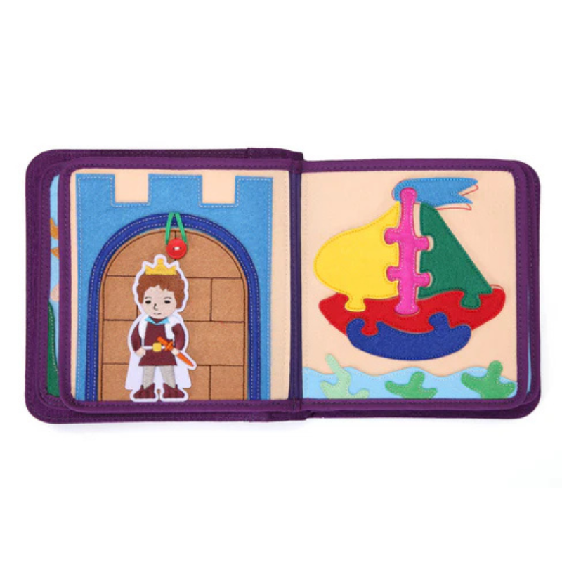 Märchenwelten Quiet Book Doppelseite: links Burgtor mit Prinz und Krone unter dem Torbogen samt Knopf-Mechanik, rechts buntes Segelboot aus abnehmbaren Filz-Puzzleteilen auf dem Meer – fördert Zuordnen. Ab 1 Jahr.