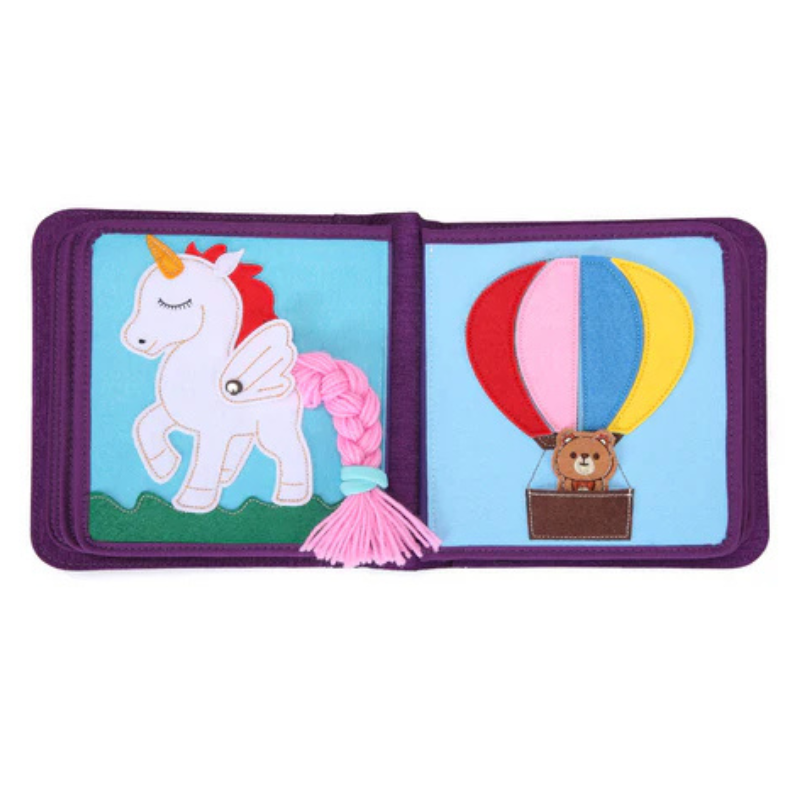 Märchenwelten Quiet Book Doppelseite: links weißes Einhorn mit Druckknopf-Flügel und dicker pinker Mähne zum Flechten, rechts bunter Heißluftballon aus Filz mit Bär im Korb – schult Flechten und Feinmotorik. Ab 1 Jahr.